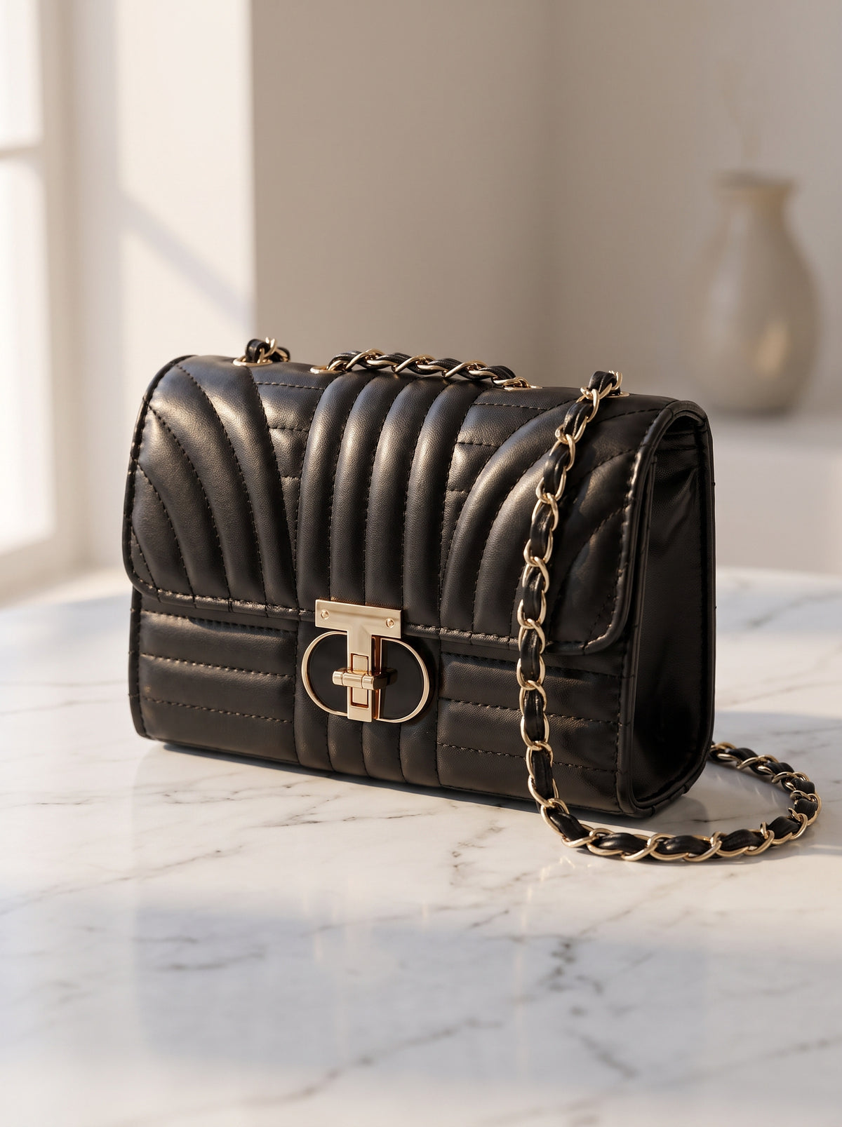 Bolso acolchado con cadena en negro sobre mármol blanco, vista de tres cuartos