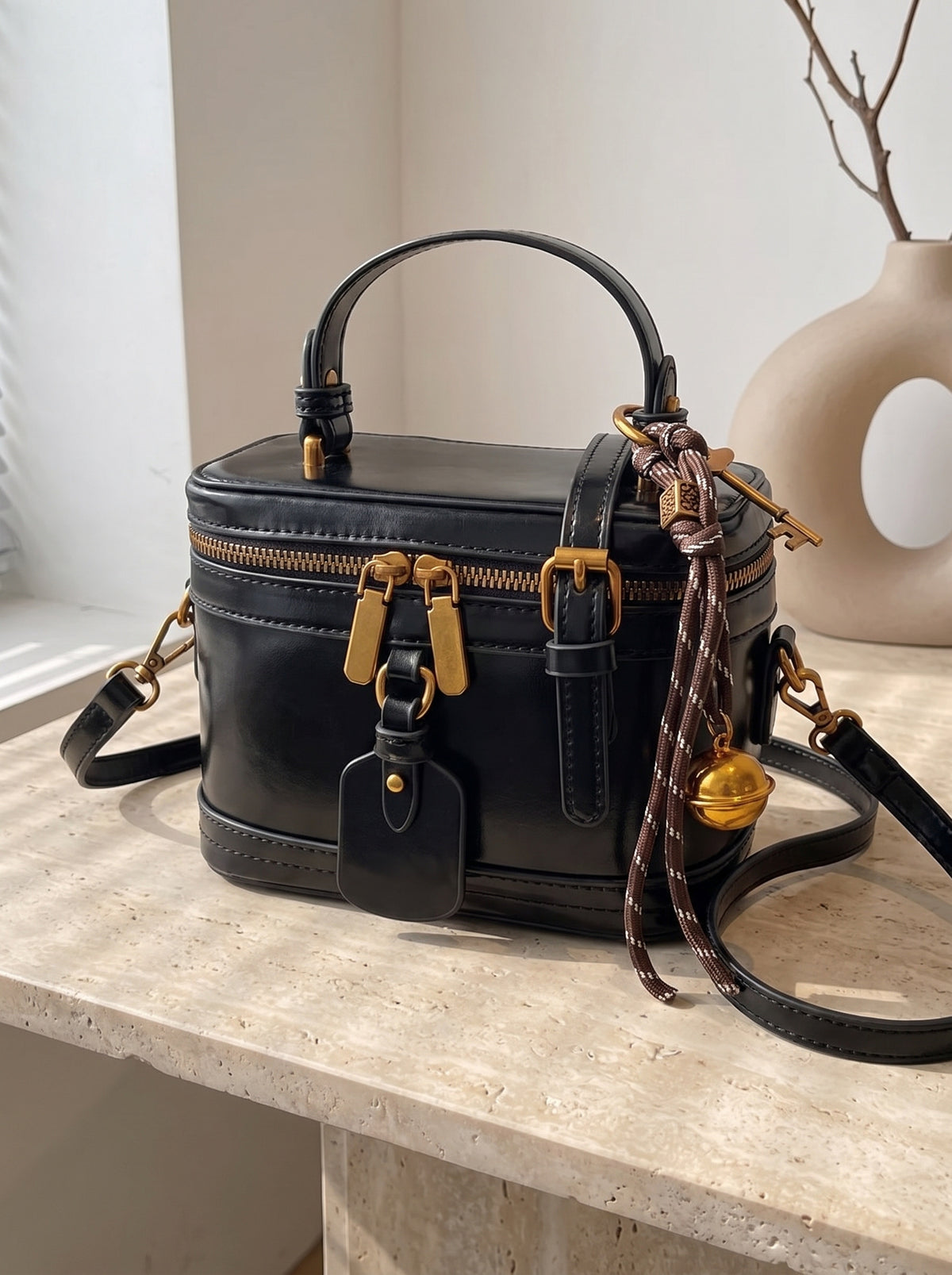Bolso neceser de piel con asa en negro sobre travertino, vista de tres cuartos