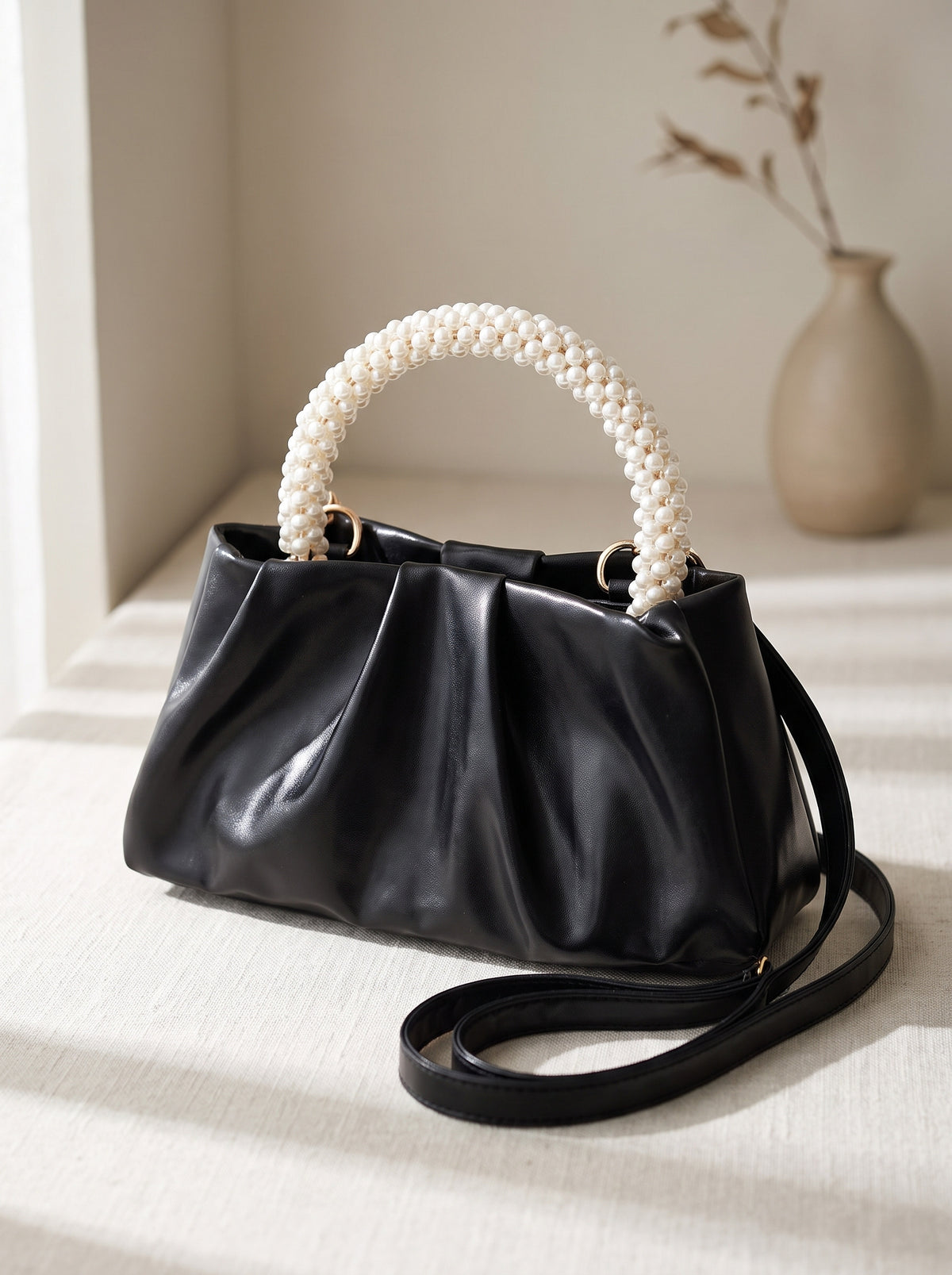 Bolso fruncido con asa de perlas en negro sobre lino, vista de tres cuartos
