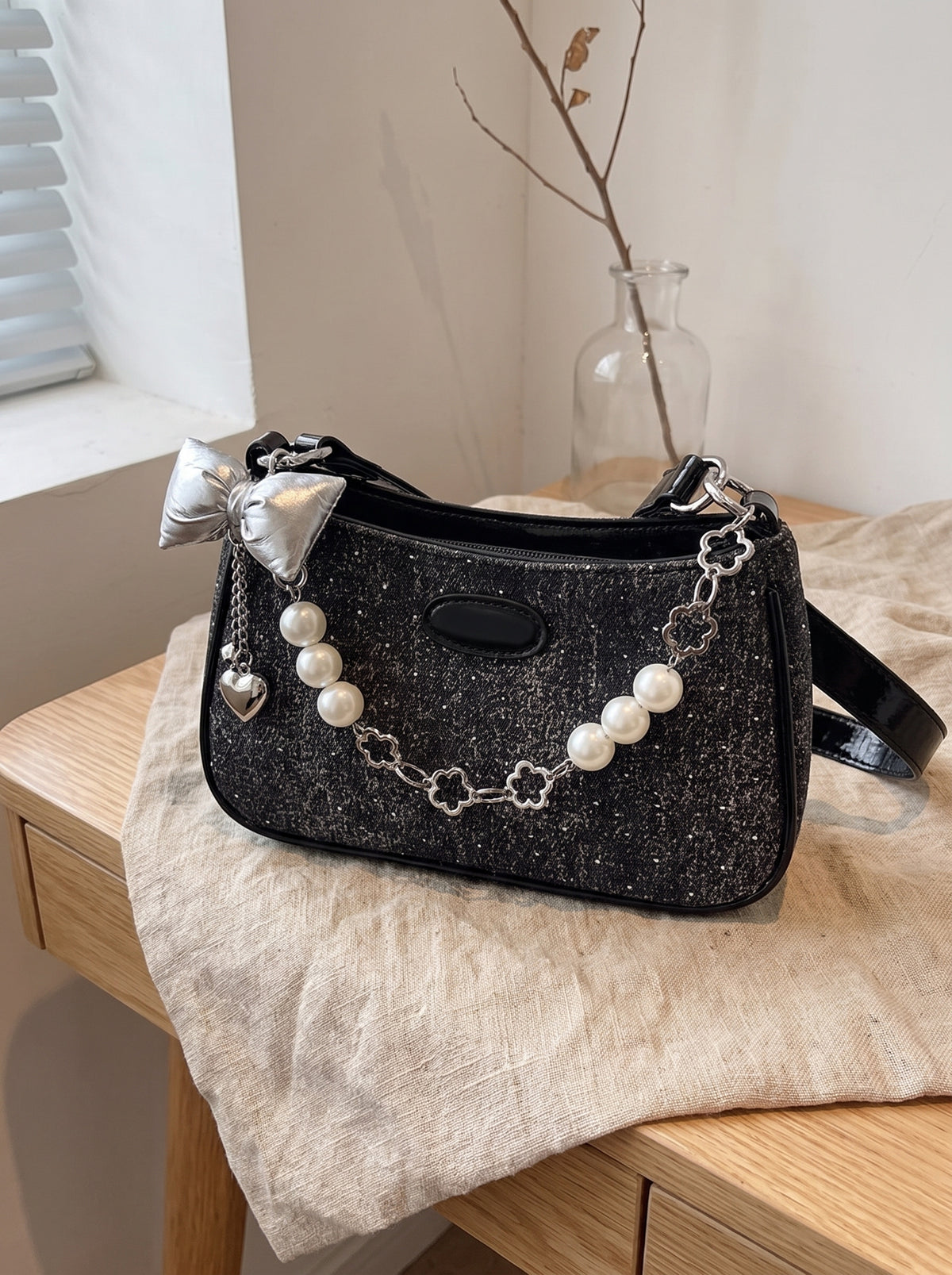 Bolso baguette con cadena de perlas en negro sobre lino, vista de tres cuartos