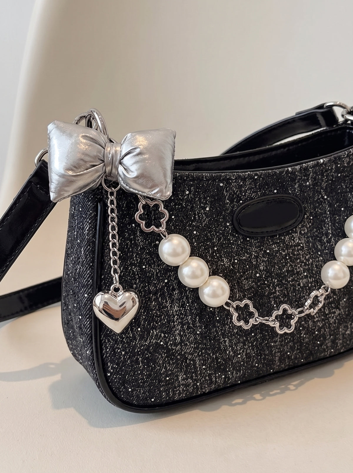 Detalle de las perlas, el lazo y la cadena de flores del bolso baguette negro